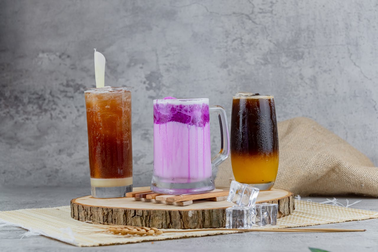 A collection of assorted beverages including coffee and a pink drink, served on a rustic board with ice cubes.